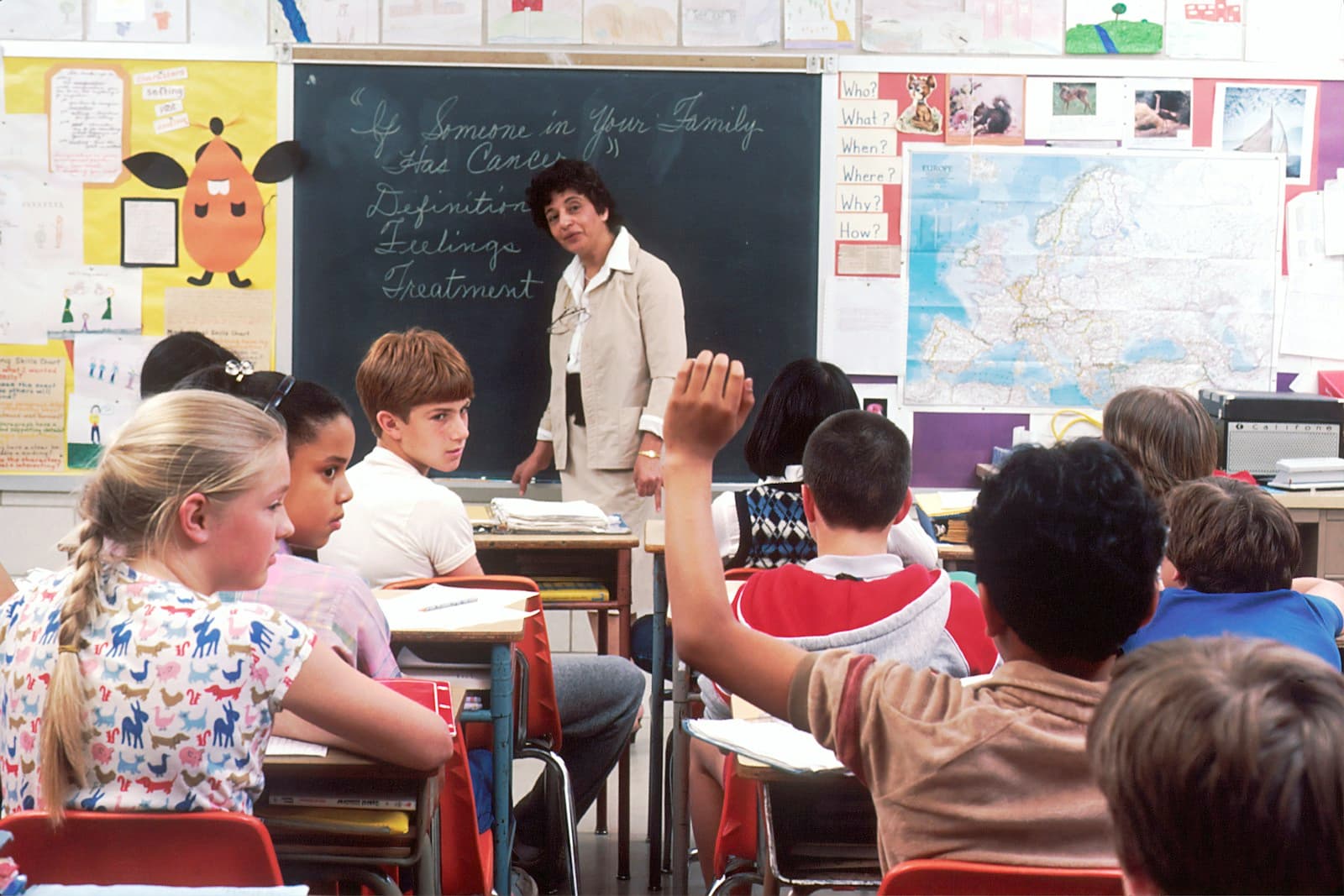 A teacher standing in front of her class as students raise their hands