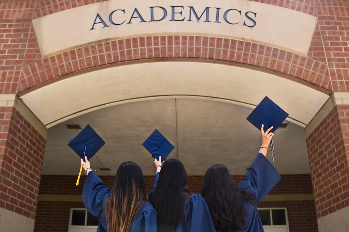 Three graduates raising their caps outside a university building